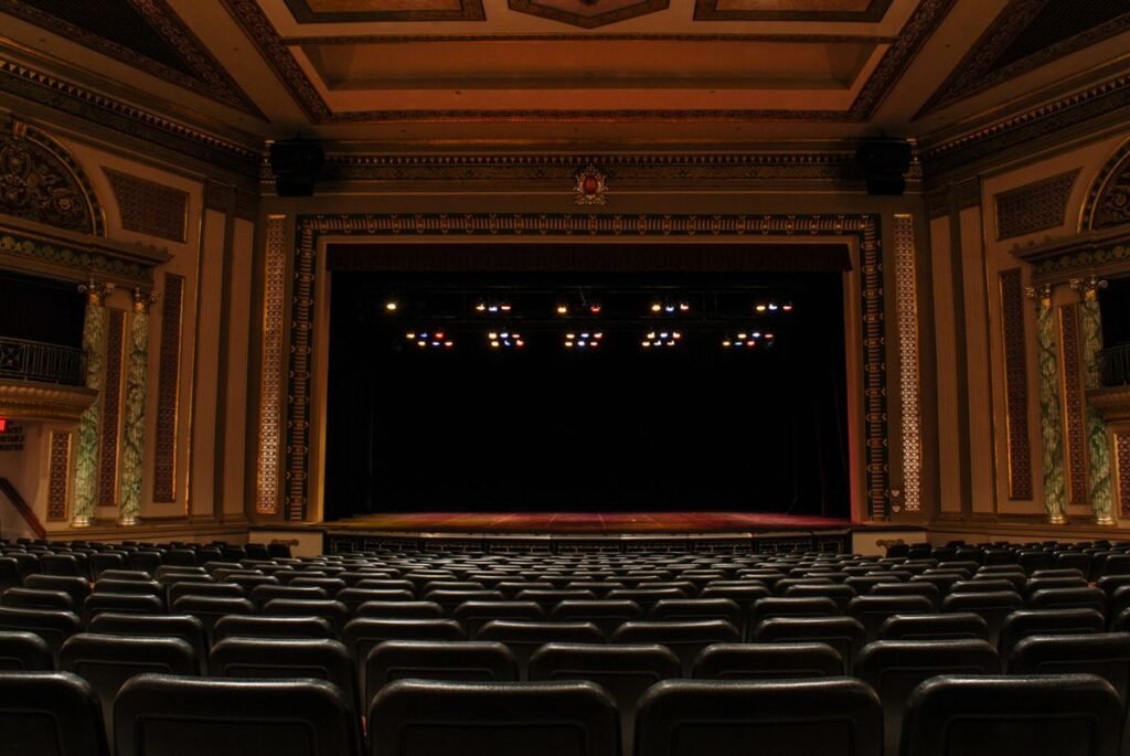 Empty ornate theater auditorium with red seats and a lit stage
