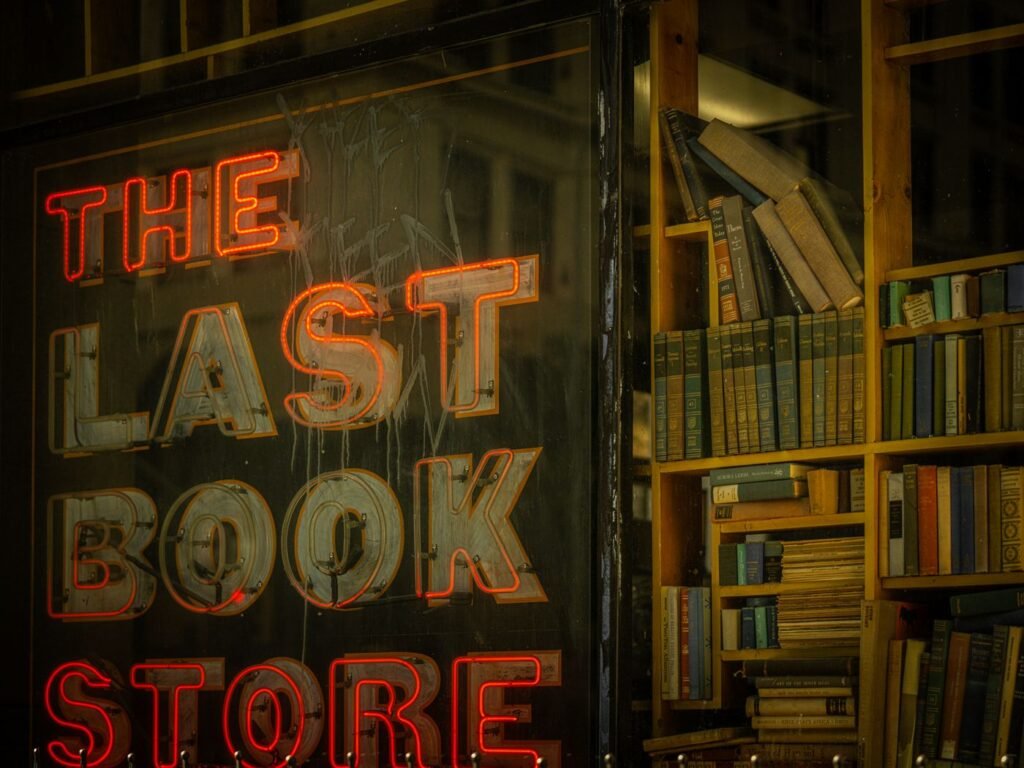 A neon bookshop sign above stacked shelves