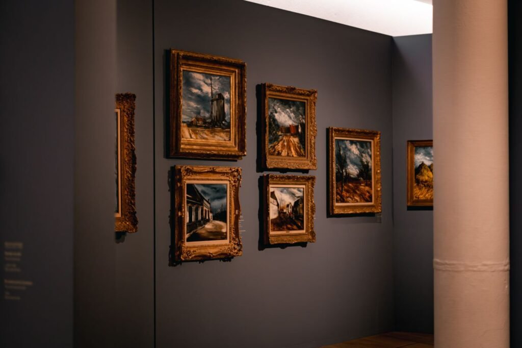 Framed paintings hung salon-style on a dark wall