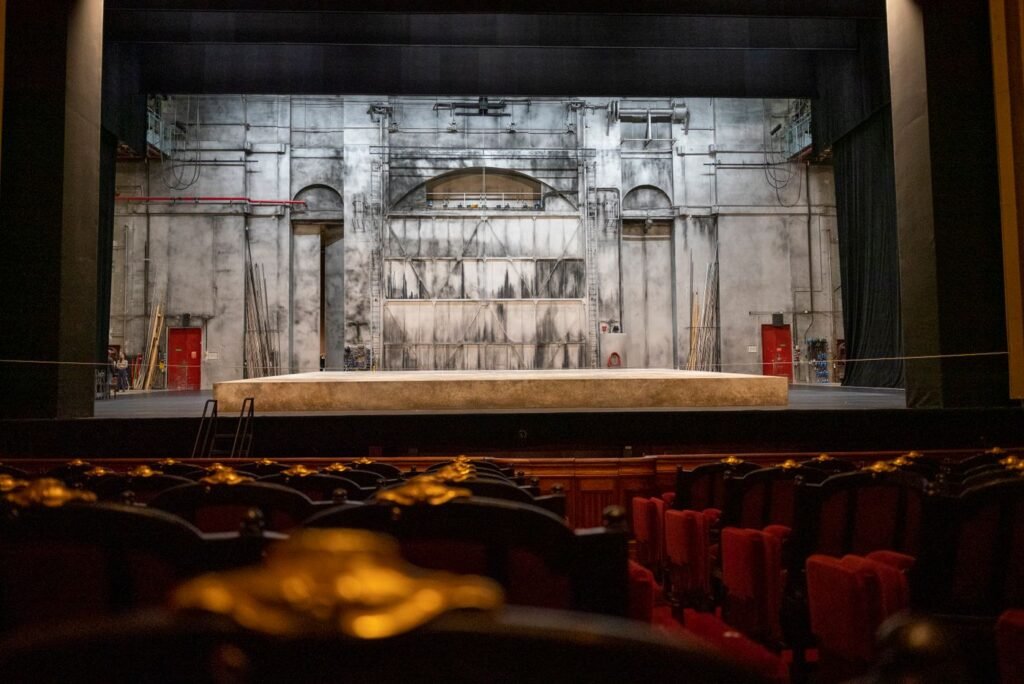 An empty theater stage with a painted backdrop and rows of seating