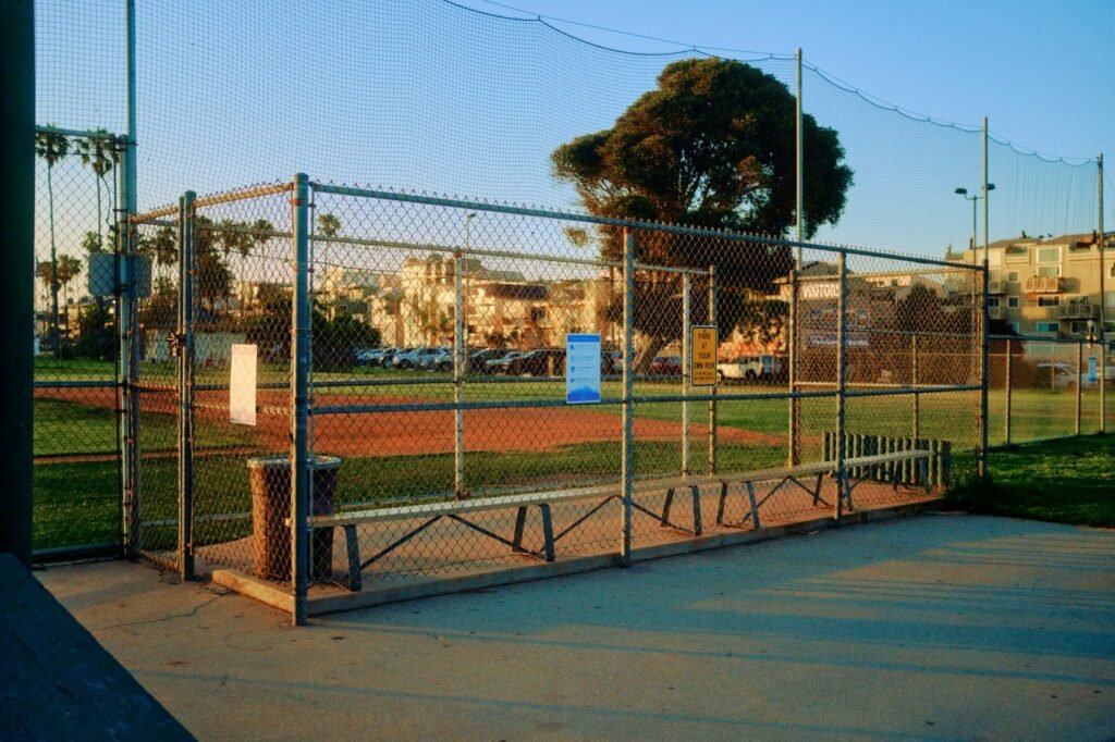An empty public baseball diamond behind a chain-link backstop at golden hour