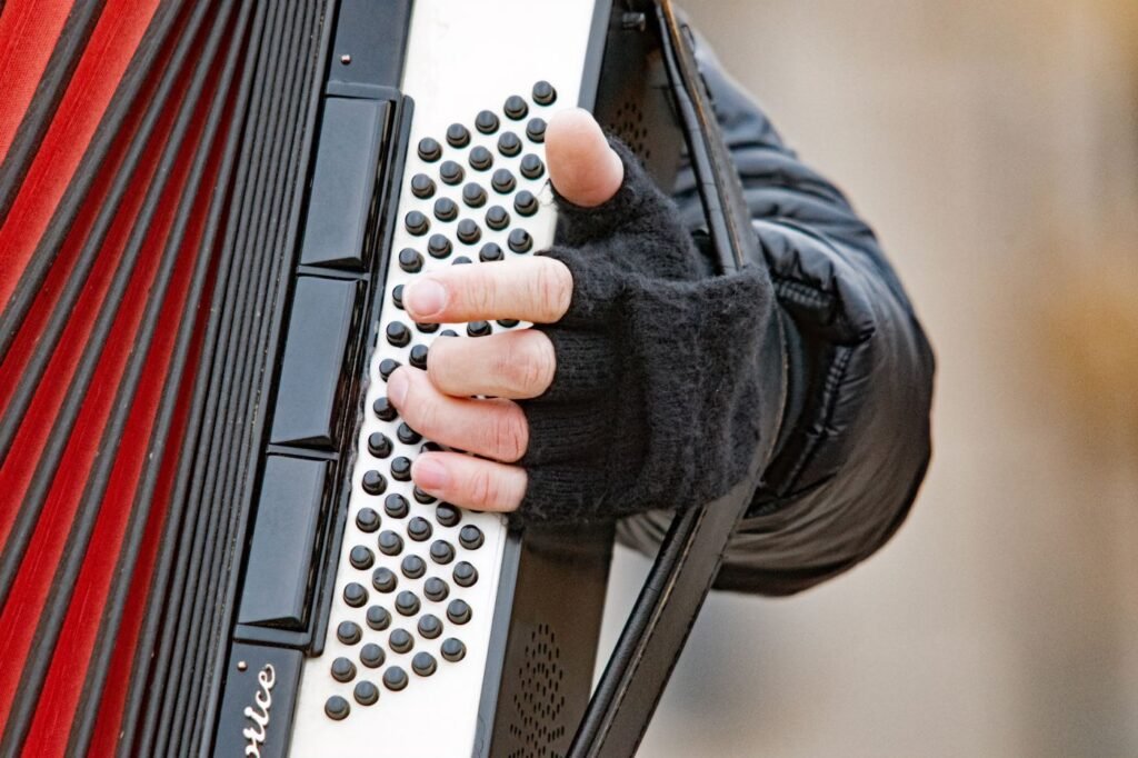 A hand in a fingerless glove playing the button side of a red accordion