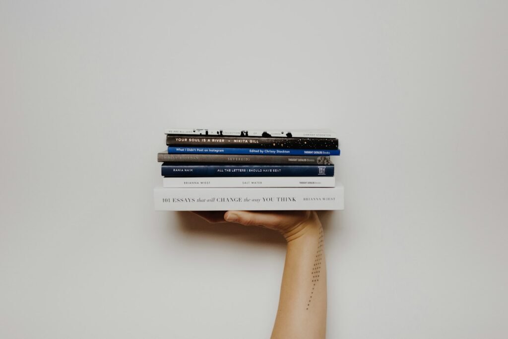 A person holding up a tall stack of books against a white wall
