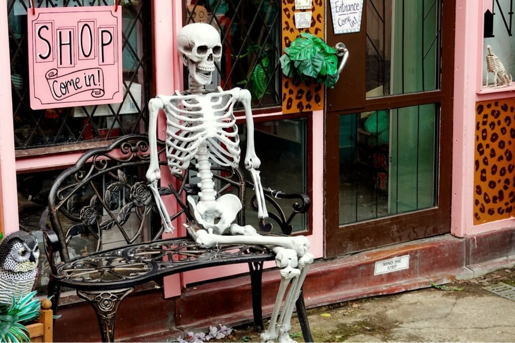 Halloween skeleton sitting on a bench outside a pink shopfront