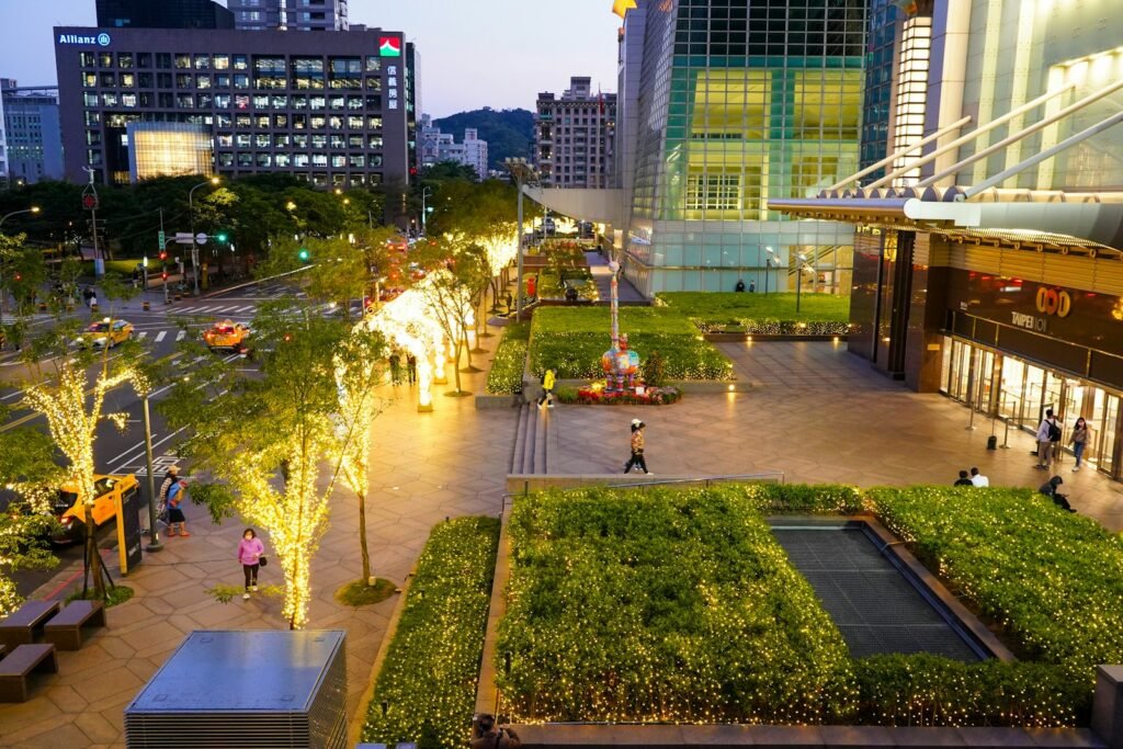 A landscaped city plaza with trees strung with lights at dusk, seen from above