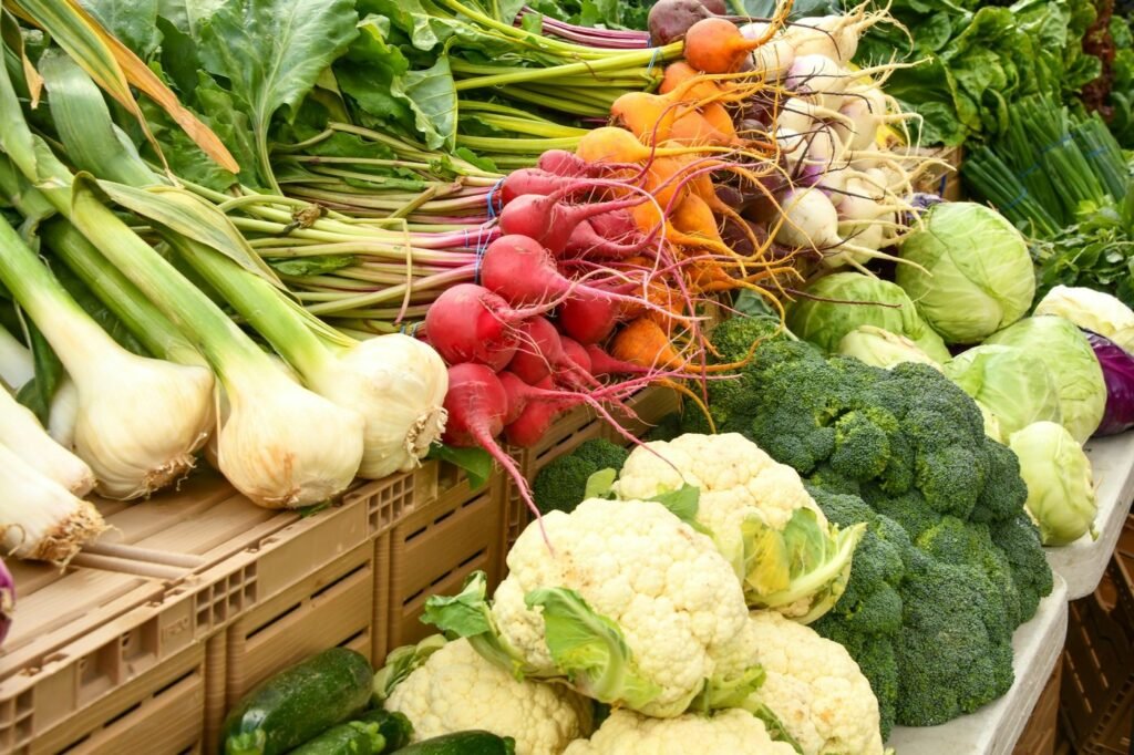A market stall piled with fresh radishes, spring onions, cauliflower, broccoli and cabbages.