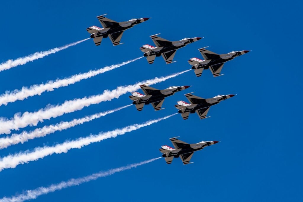 Six fighter jets in tight formation with white smoke trails against a deep blue sky.