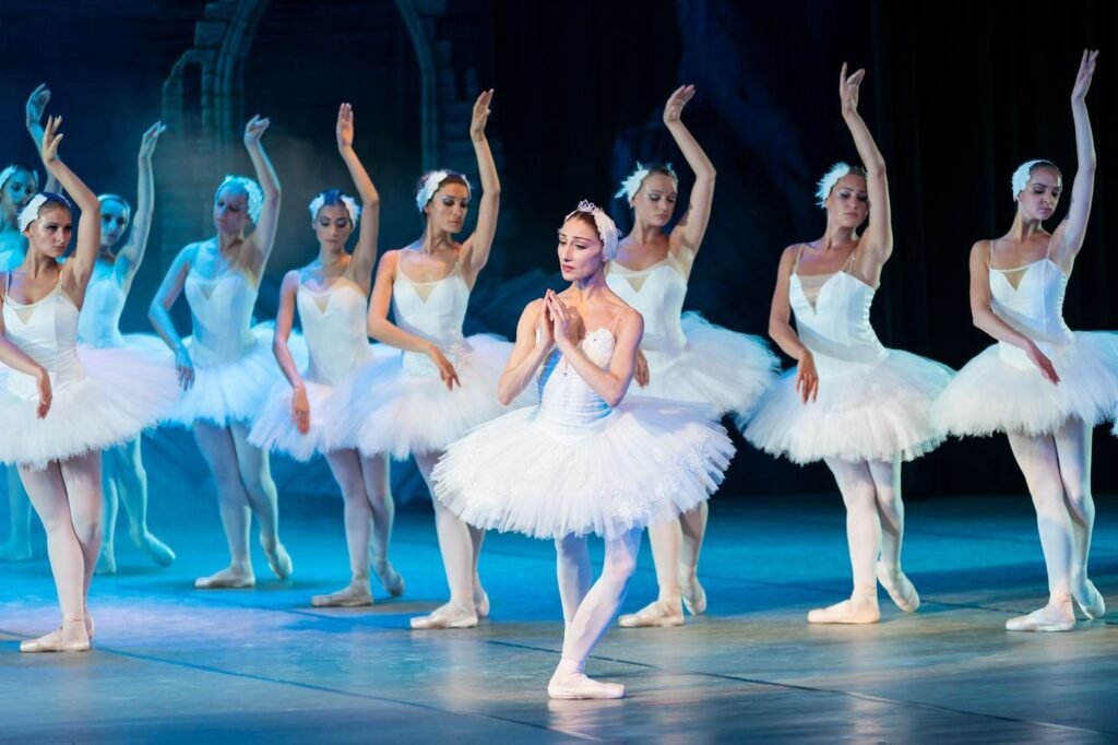 A line of ballerinas in white tutus performing on a lit stage.
