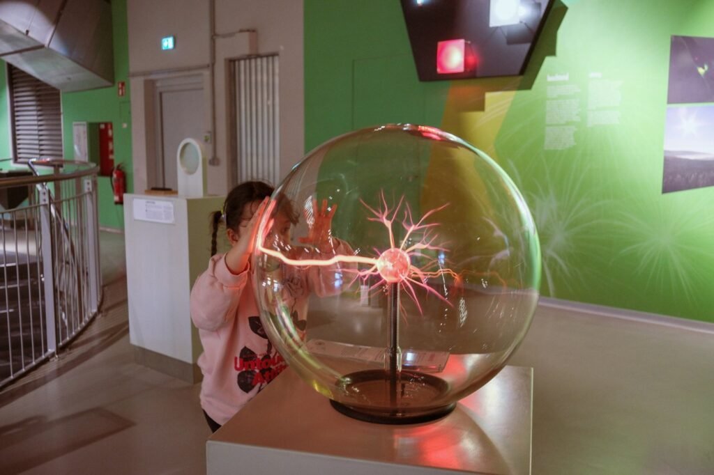 A child touches a glowing plasma ball at a hands-on science museum exhibit.