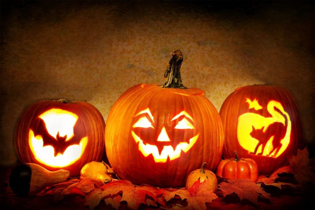 Three glowing carved Halloween jack-o-lanterns among autumn leaves.