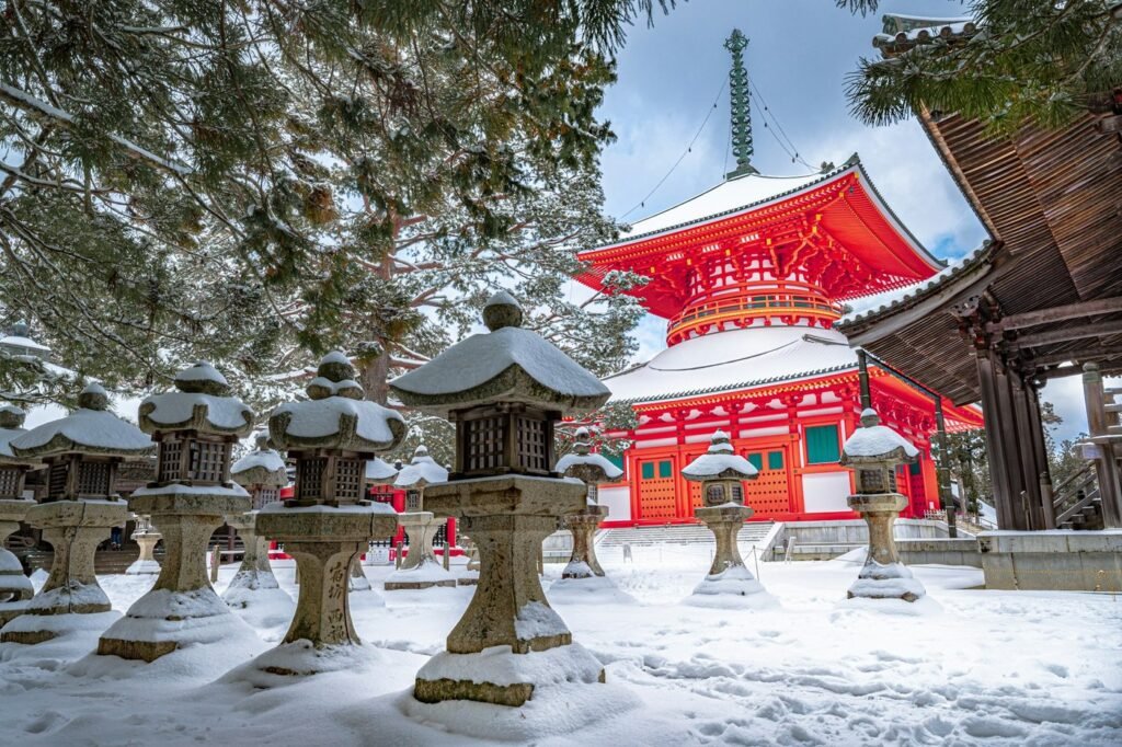 A red Japanese temple pagoda and stone lanterns covered in winter snow.