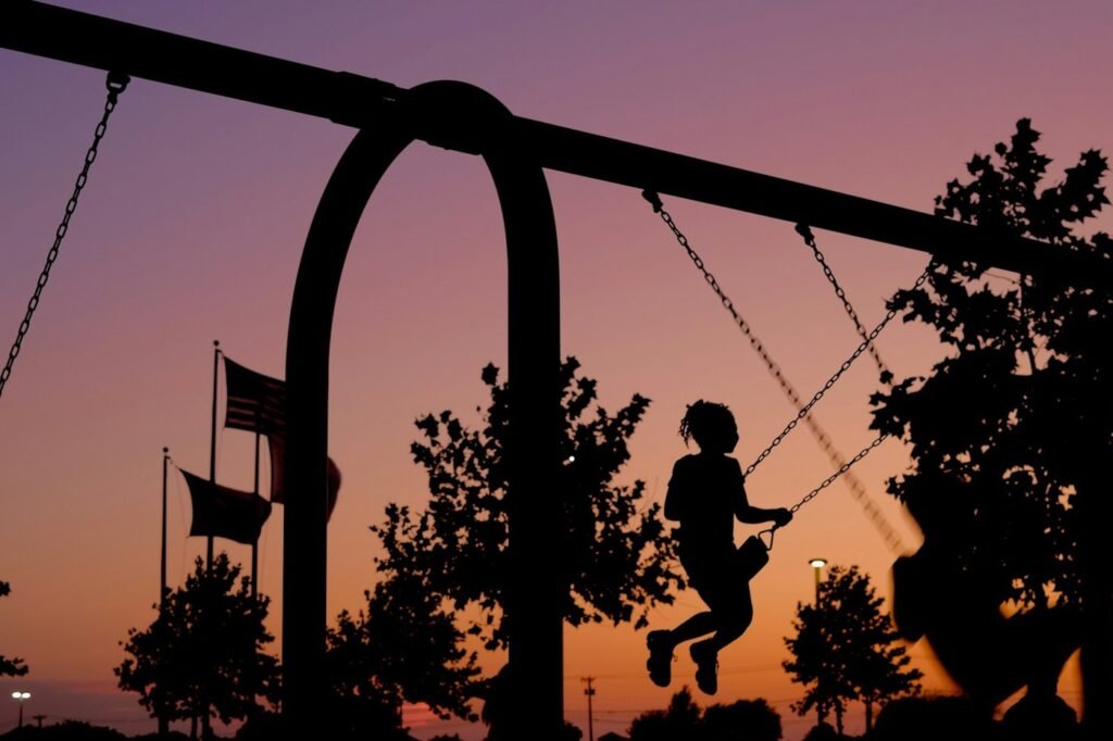 Silhouette of a child on a playground swing against a sunset sky.