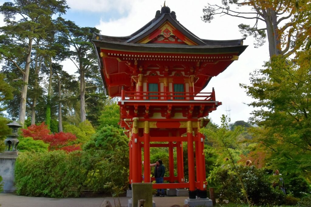 A red pagoda gate among tall trees and autumn foliage in a landscaped garden park.