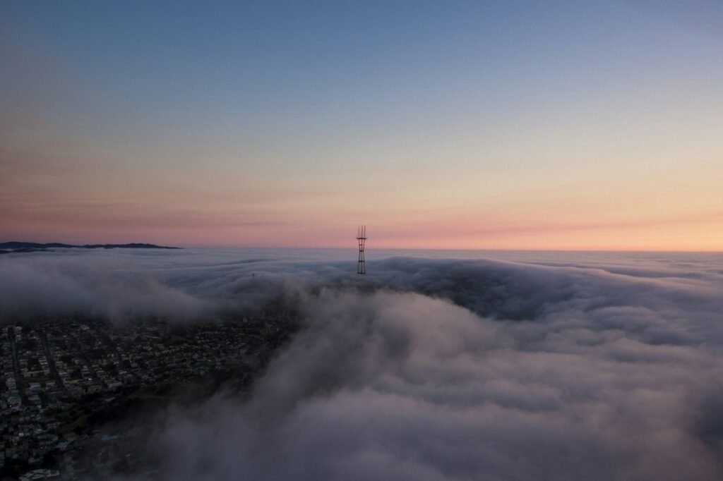 Sutro Tower rising above a bank of fog over San Francisco at dusk.
