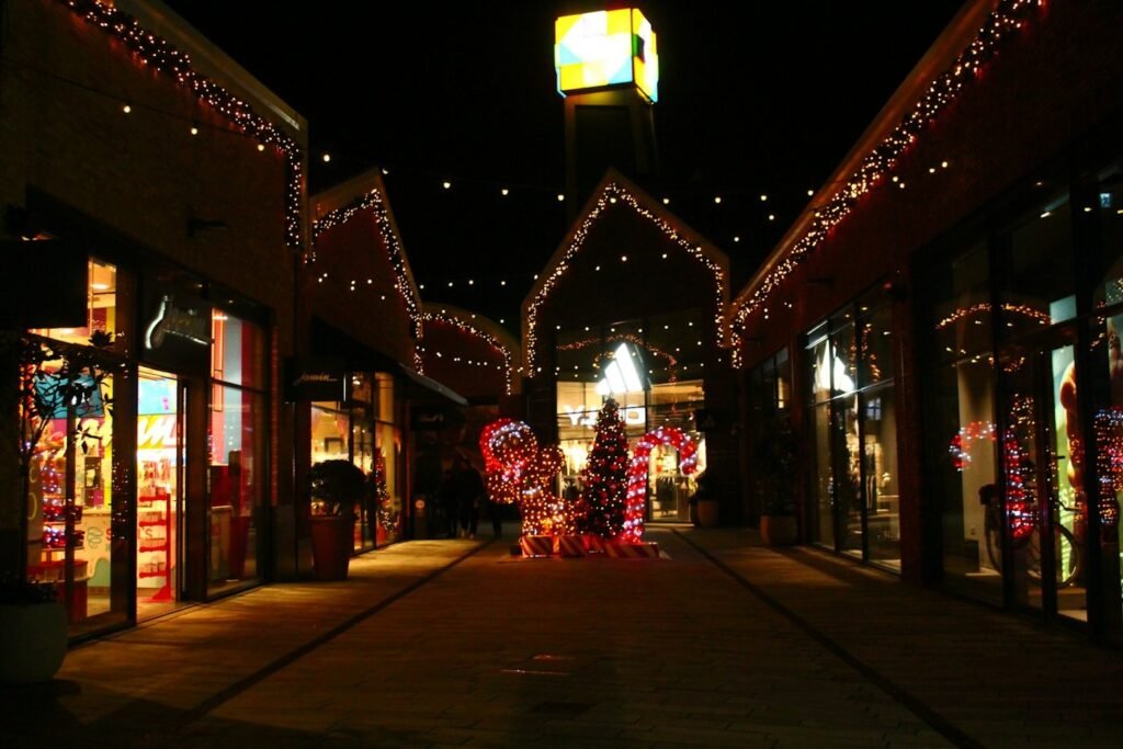 A shopping street at night with strings of holiday lights, a decorated tree and candy-cane lights