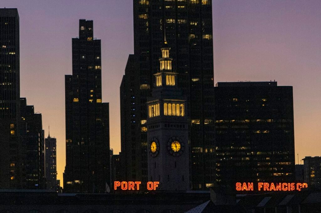 The Ferry Building clock tower and downtown San Francisco towers at dusk, with the Port of San Francisco sign lit