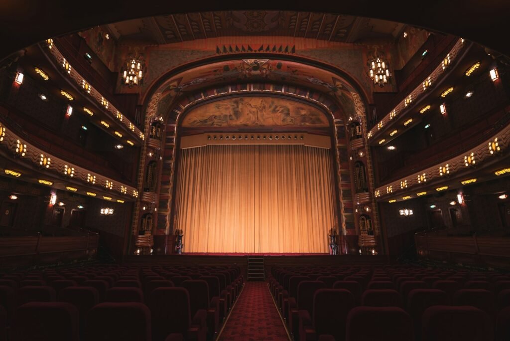 The warmly lit interior of a historic theater with balconies and a closed stage curtain