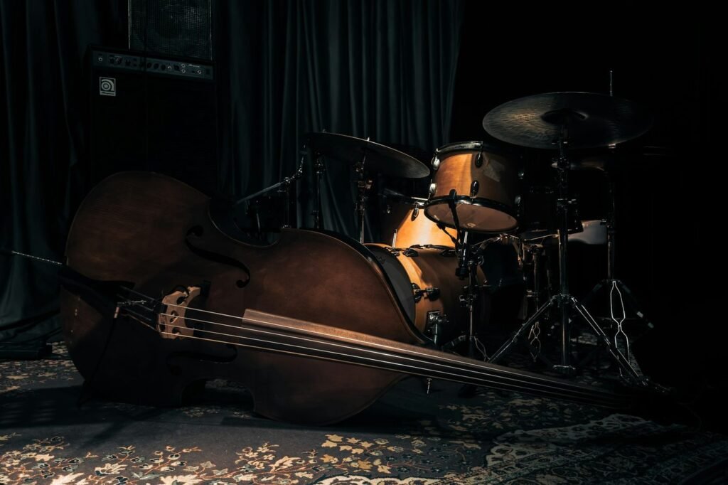 An upright bass lying on a rug in front of a drum kit on a dark stage