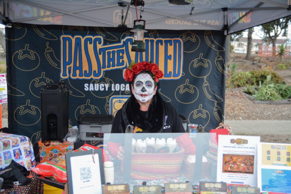 A vendor in Dia de los Muertos face paint and a flower crown at a sauce stand at the Outer Sunset Farmers Market and Mercantile