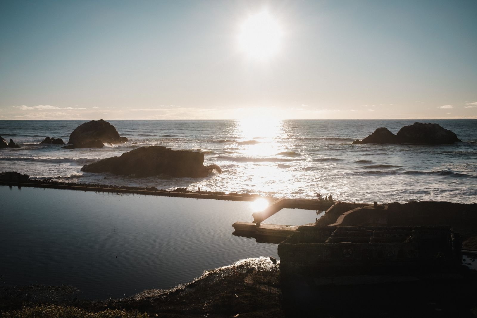 The sun low over the ocean with rocks near Sutro Baths.