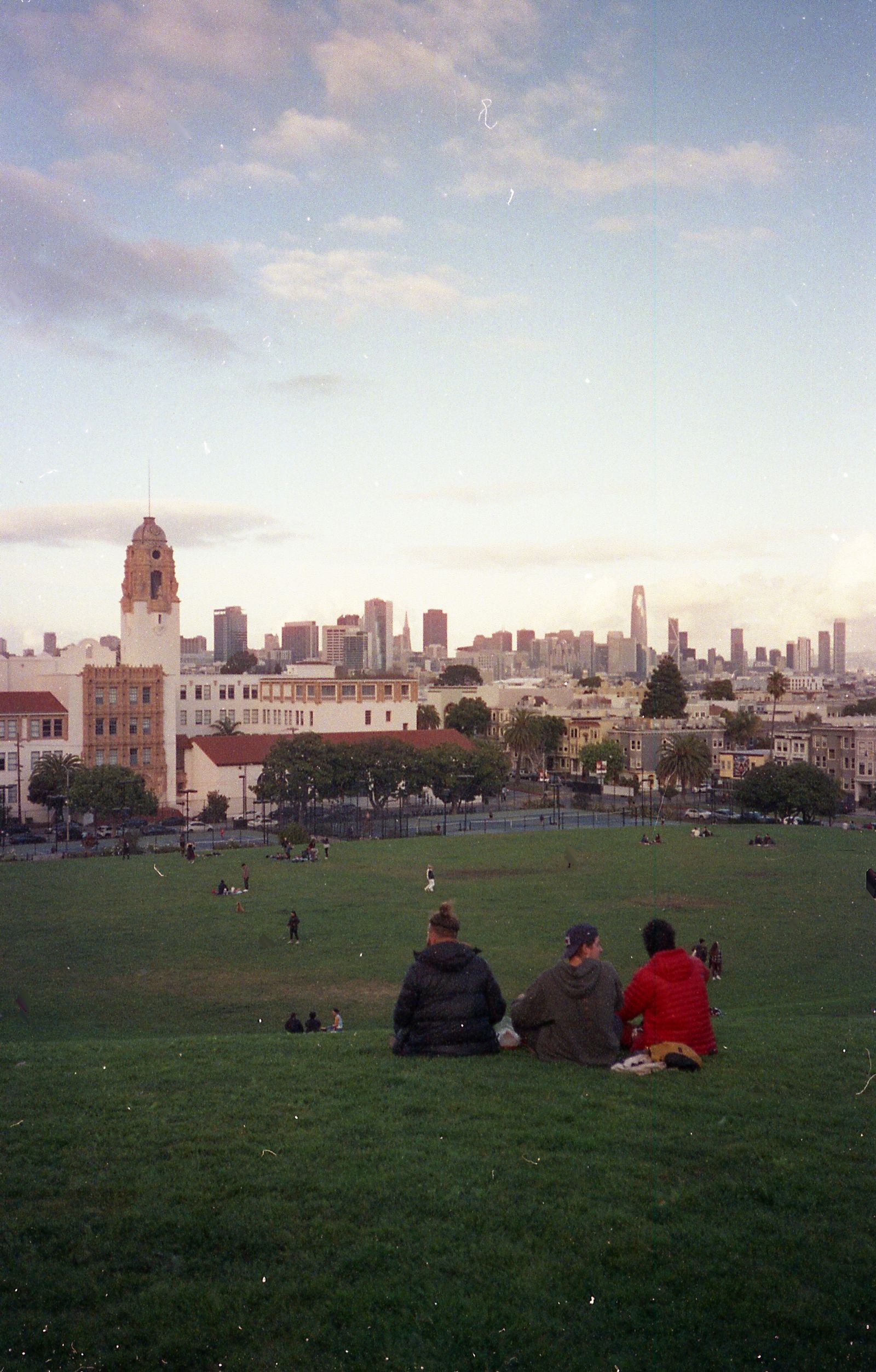 People sitting on the lawn at Dolores Park with the skyline behind.