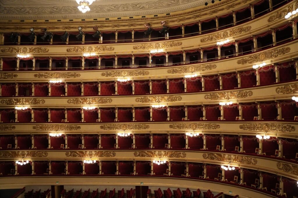 Gilded boxes and red velvet seats inside a historic opera house.