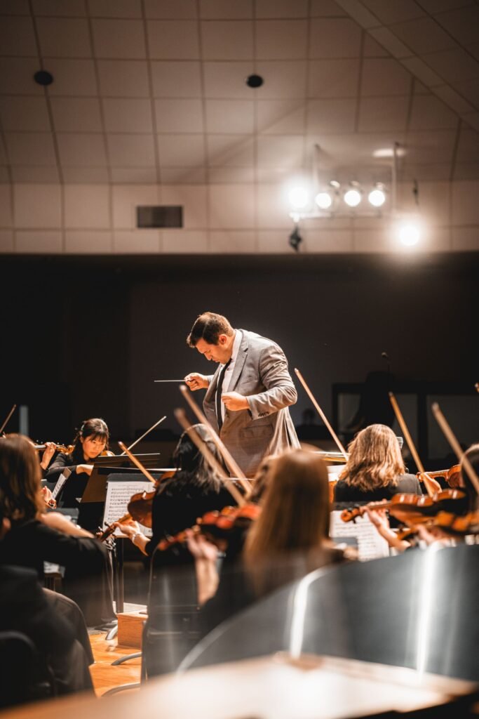 A conductor leading a string orchestra under stage lights.