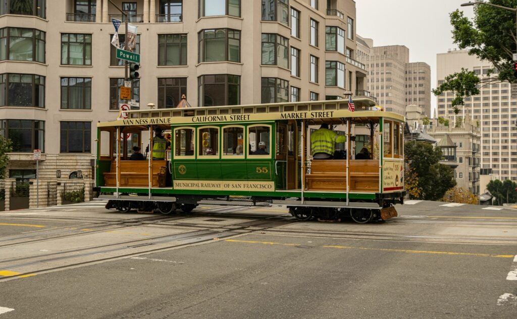 A green and cream San Francisco cable car number 55 crossing Powell Street on the California Street line