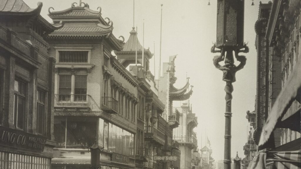 Historic photograph of a San Francisco Chinatown street with pagoda-style rooftops, an ornate lamp post and parked cars