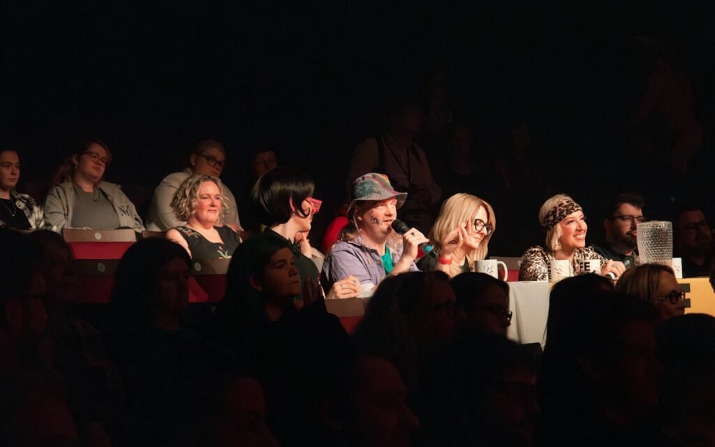 An audience seated in a dark room listening to speakers at an evening reading