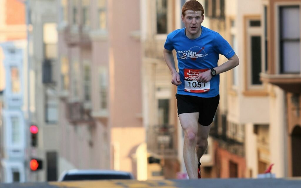 A runner in a race bib on a city street lined with row houses