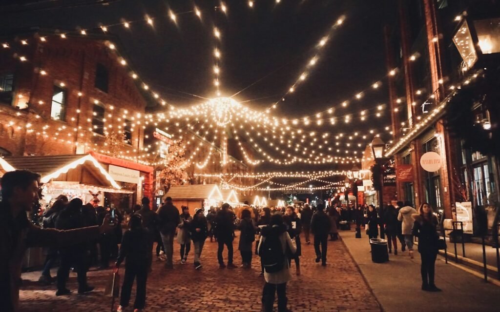An evening street with strings of warm lights overhead and people walking