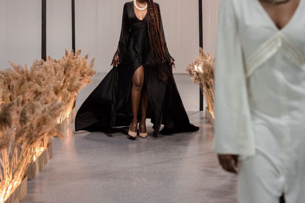 Models in long gowns walking an indoor runway lined with lit pampas grass
