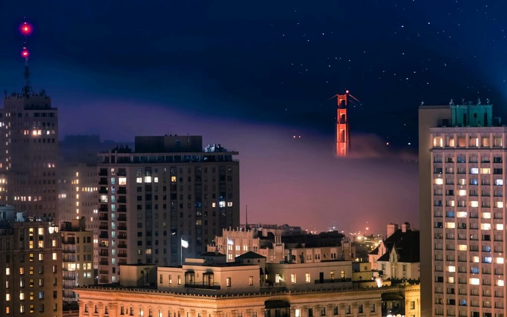 Fog drifting over San Francisco's skyline at night, with a red-lit bridge tower rising above it