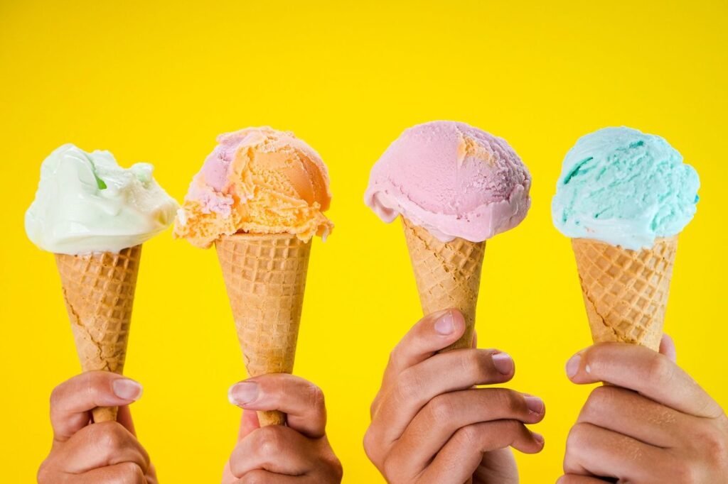 Four colorful scoops of ice cream in waffle cones against a yellow background