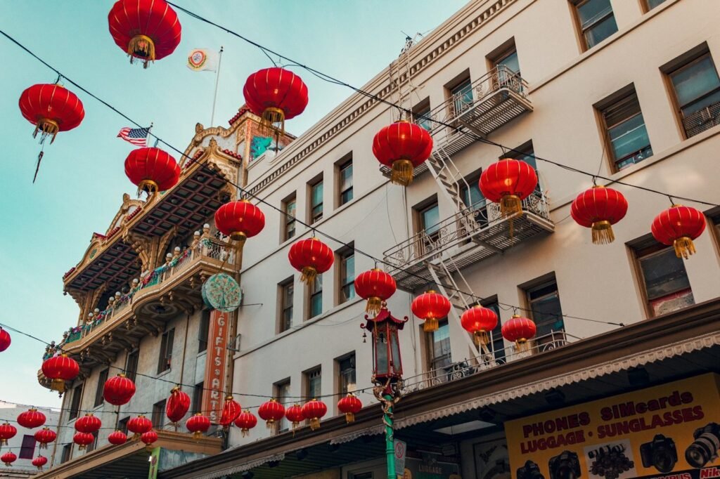 Red paper lanterns hanging over a Chinatown street in San Francisco, with historic buildings on both sides.