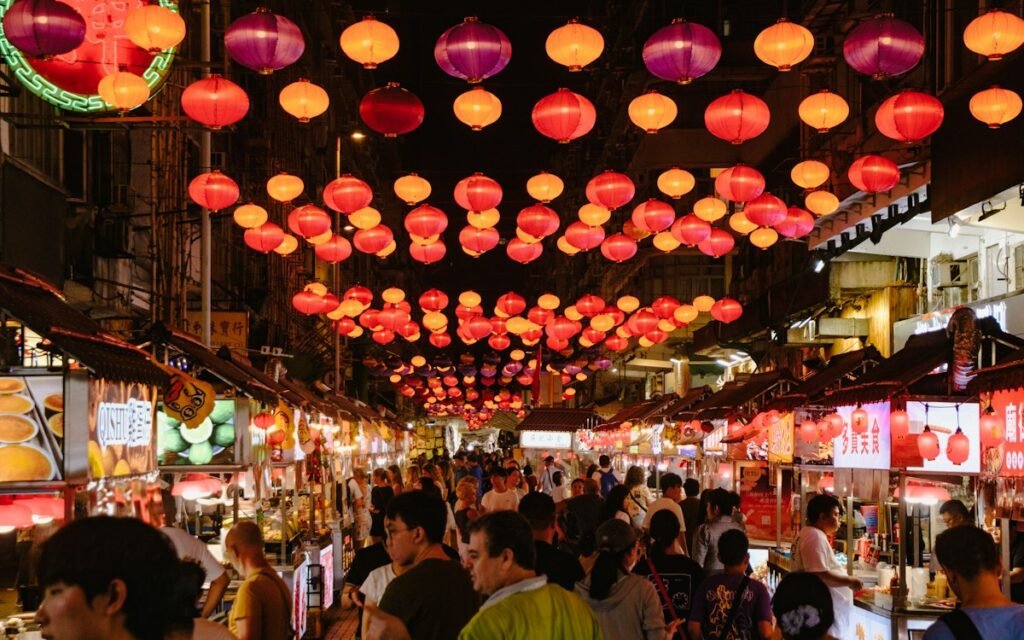 A crowded evening market street under rows of red lanterns and food stalls