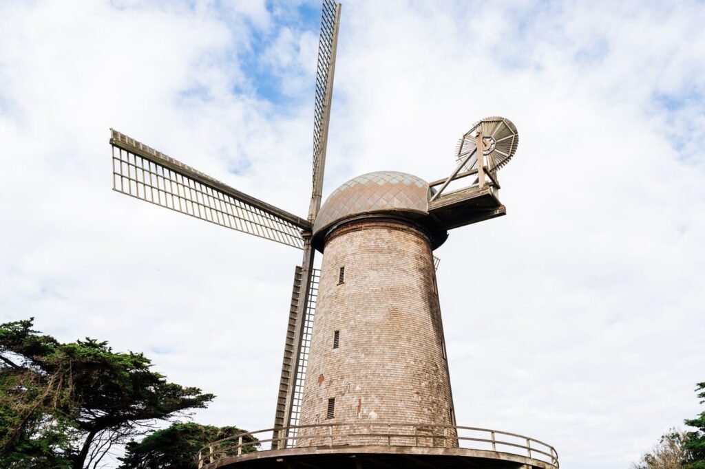 A shingled windmill with wooden sails rising above cypress trees in Golden Gate Park.