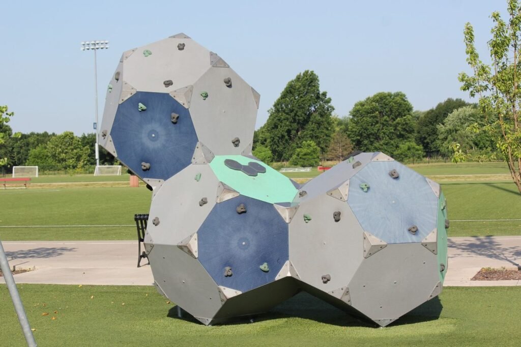 Geometric dome climbing structures on a park lawn beside a sports field