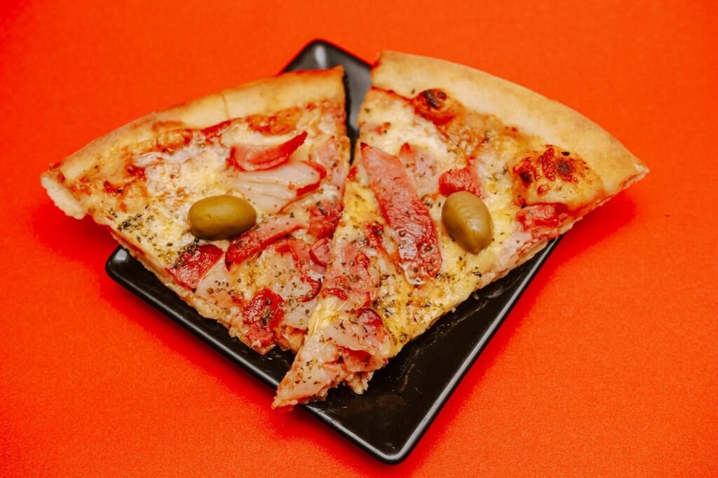 Two thin-crust pizza slices with olives on an orange background
