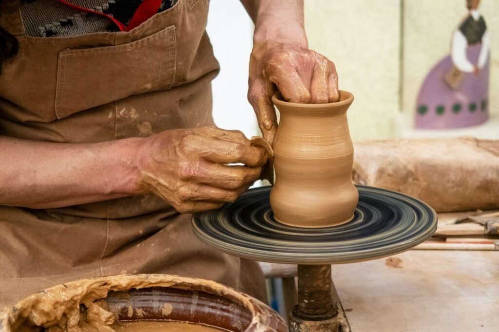Clay-covered hands shaping a small vase on a spinning pottery wheel