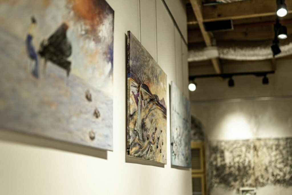 Paintings hung along a white gallery wall under track lighting