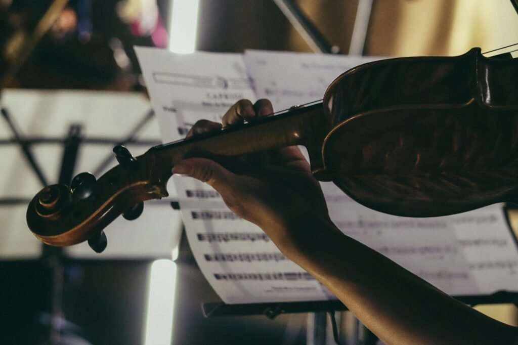 A hand on a violin's neck in front of sheet music on a stand