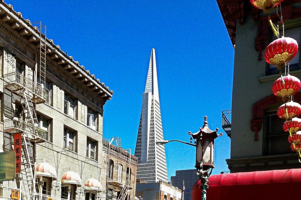 The Transamerica Pyramid rising behind a Chinatown street, with red lanterns and a pagoda-style streetlamp in the foreground
