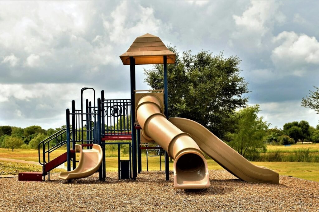An empty playground with tube slides and a climbing structure under a cloudy sky